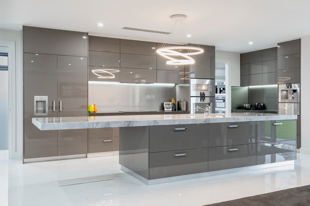 Modern kitchen with glossy grey cabinets, marble island, and a sculptural circular pendant light.