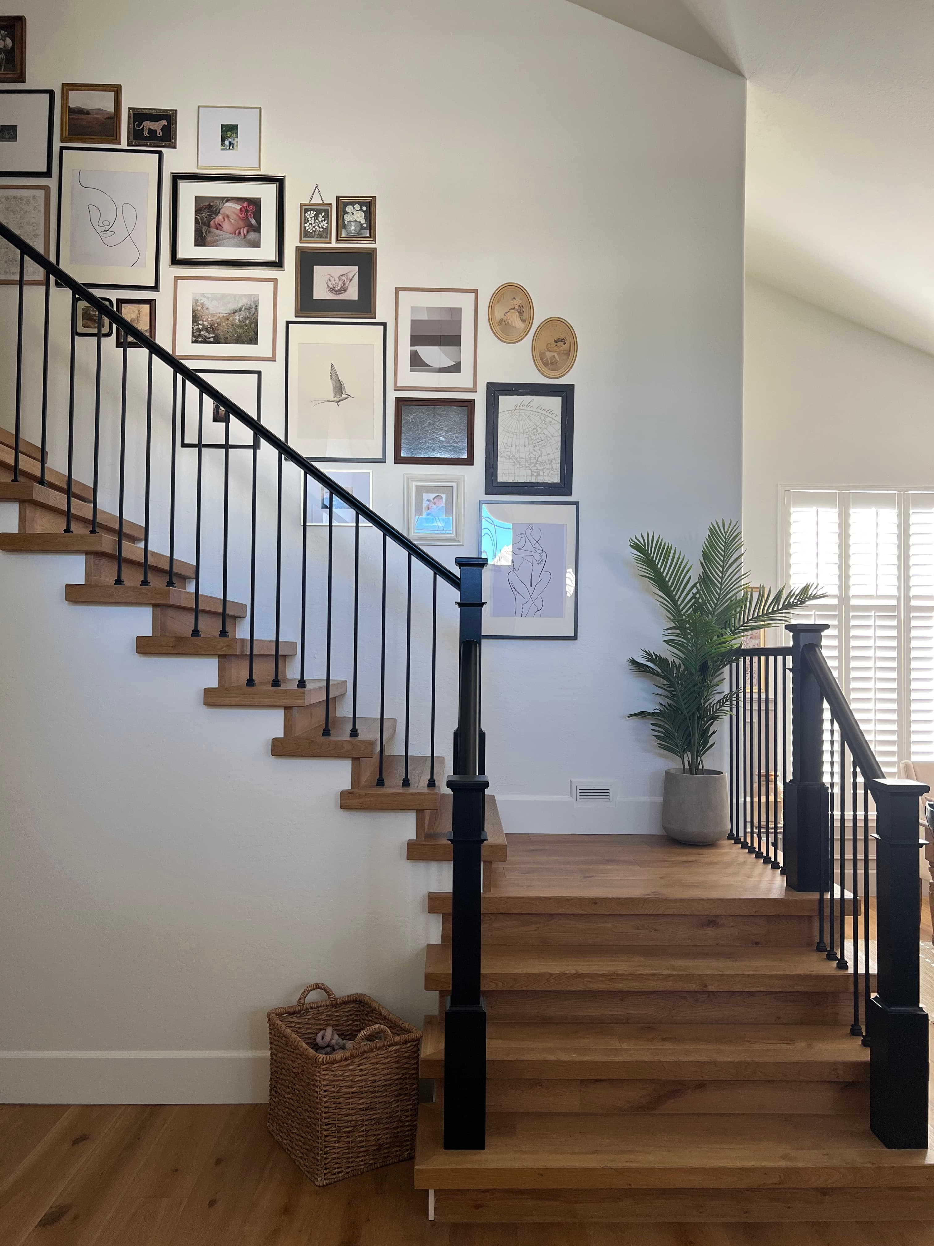 Modern wooden staircase with black railings and a gallery wall of framed art and photos.