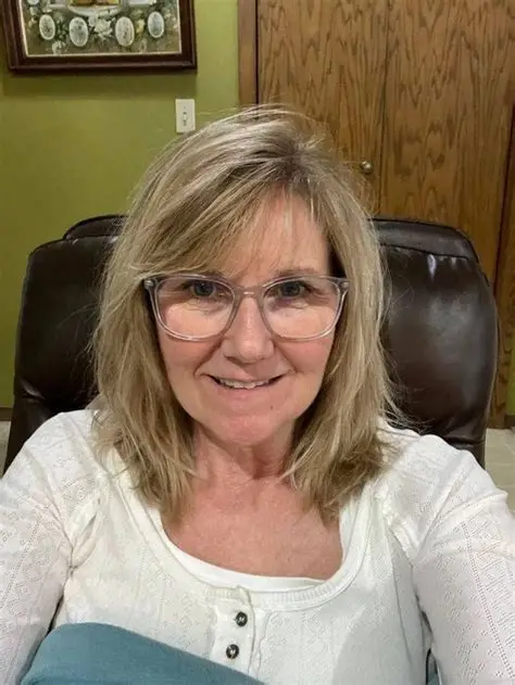 Smiling blonde woman wearing clear glasses and a white shirt in a leather chair.