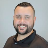 A smiling man with short dark hair and a beard wearing a black polo shirt.